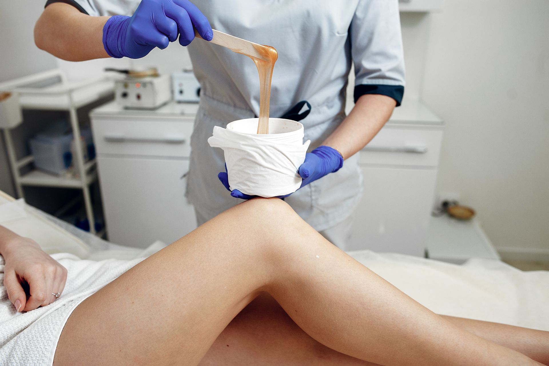 Woman's leg being waxed at a spa; a person in gloves and a uniform holds wax and applies it to the leg.