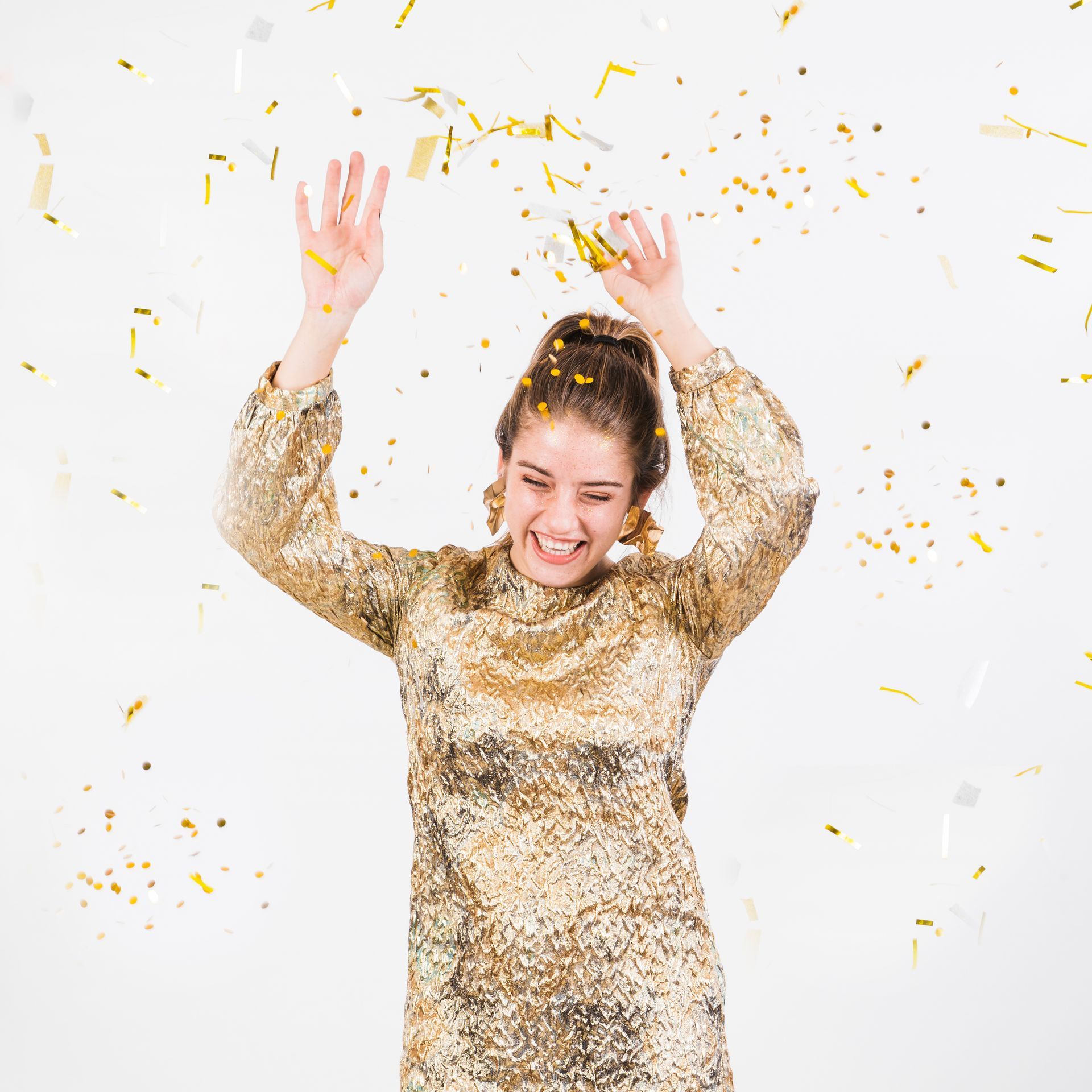 Woman in gold dress, arms raised, confetti falling, smiling, white background.