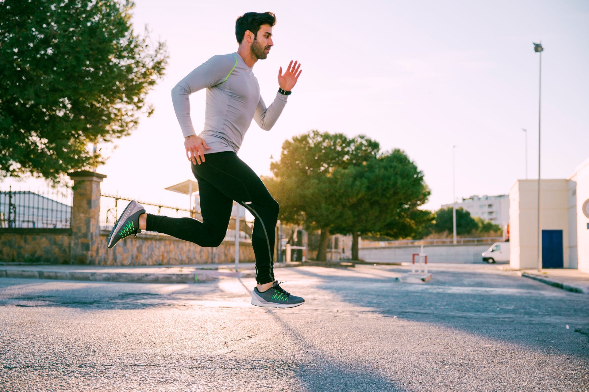 Man running on a road, wearing athletic clothes. Bright sunlight in background.