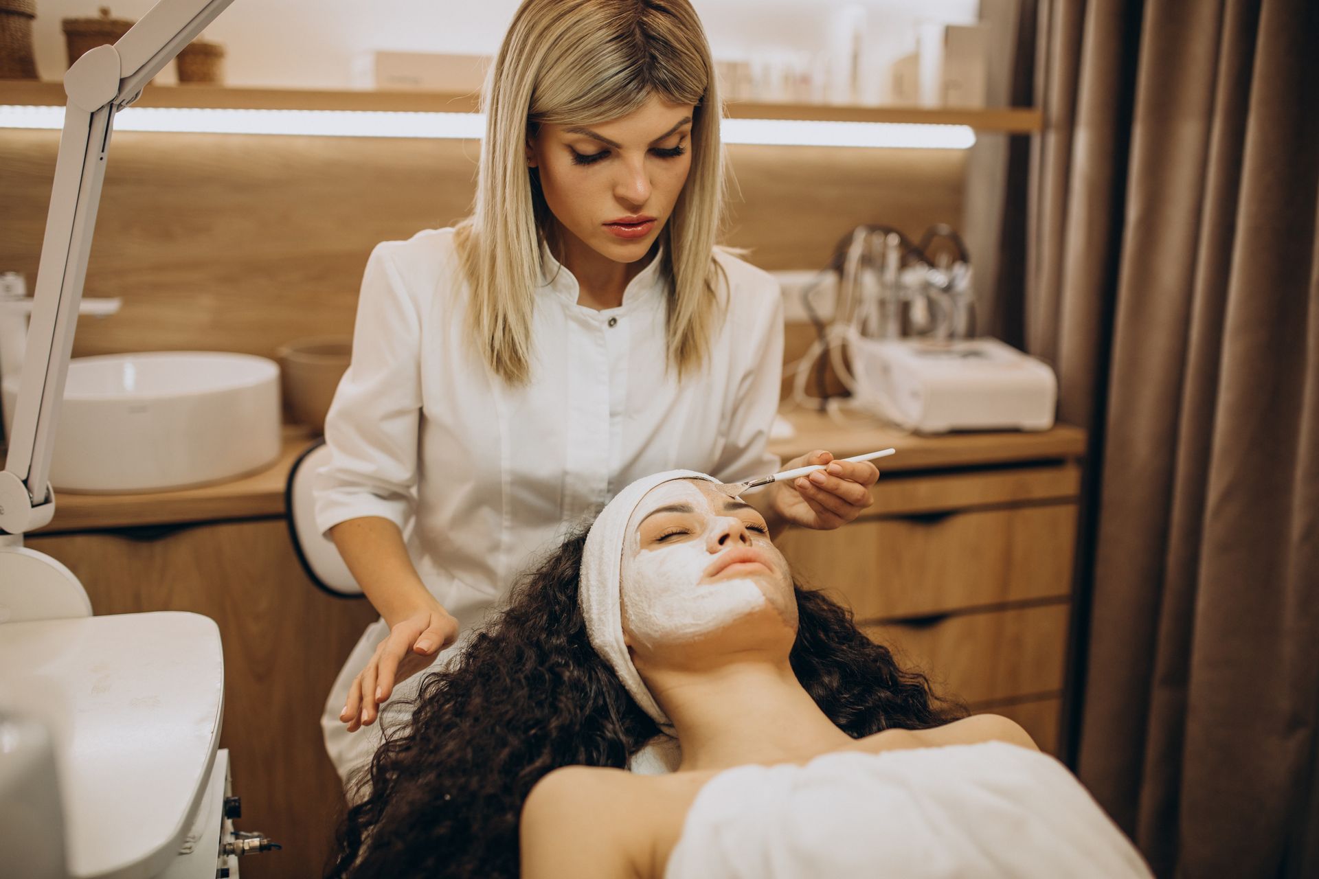 Woman receiving facial treatment in a spa. Therapist applies cream.