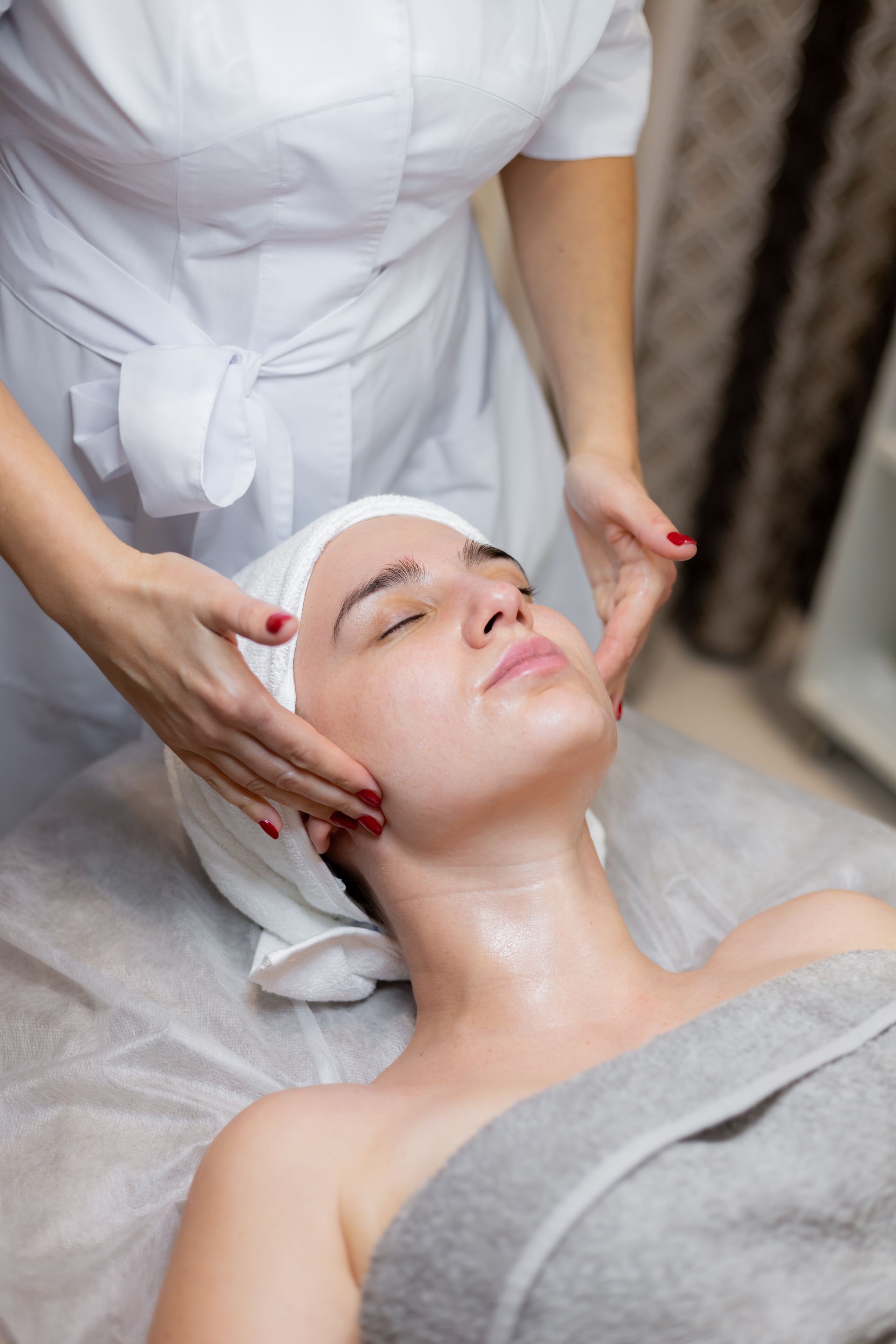 Woman receiving facial massage in a spa setting, with closed eyes and a serene expression.