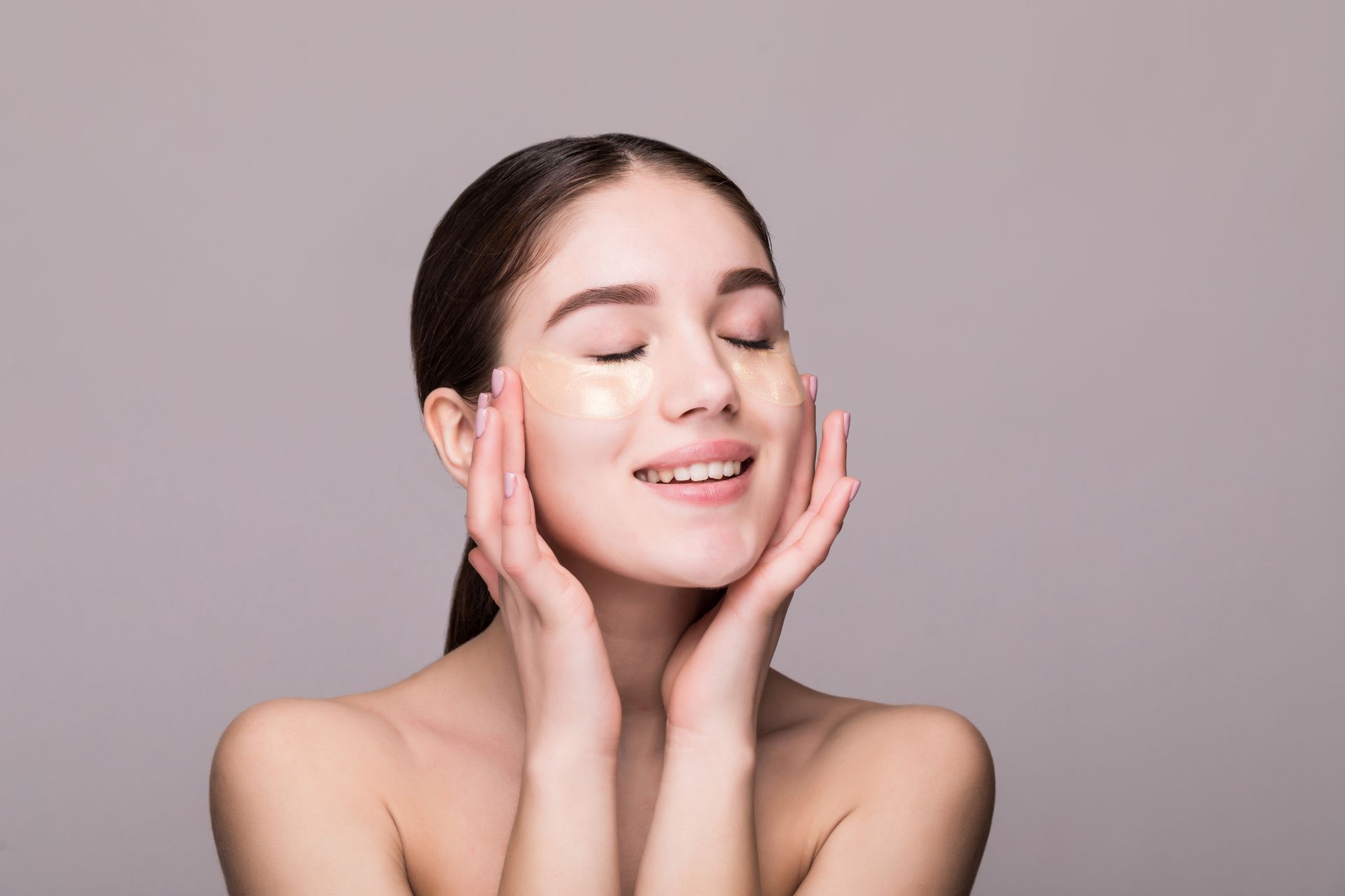 Woman with eye patches, smiling, hands on cheeks.