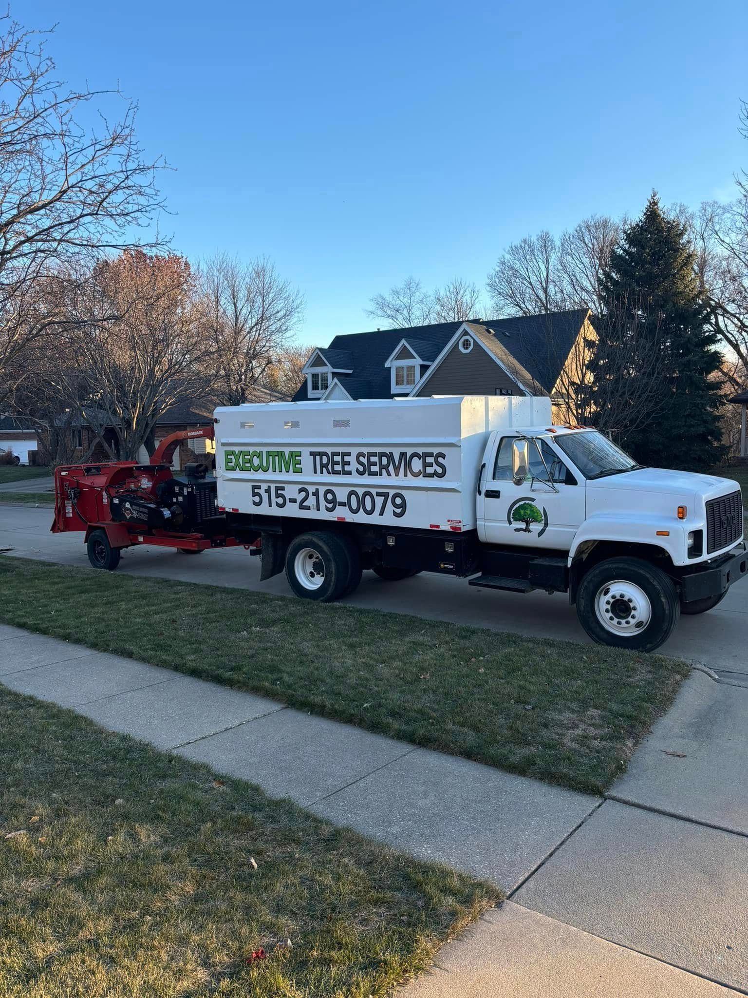 A white truck with a chipper attached to it is parked in front of a house.