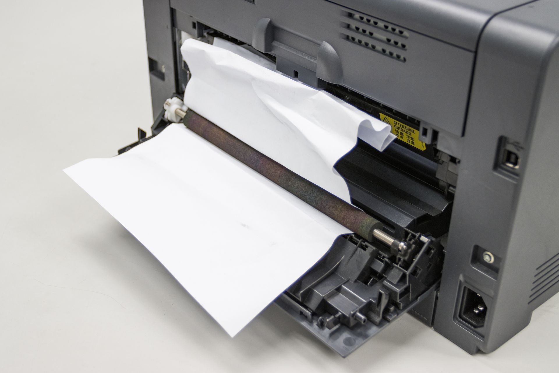 A paper jam in an open laser printer with a sheet of white paper caught on the rollers.