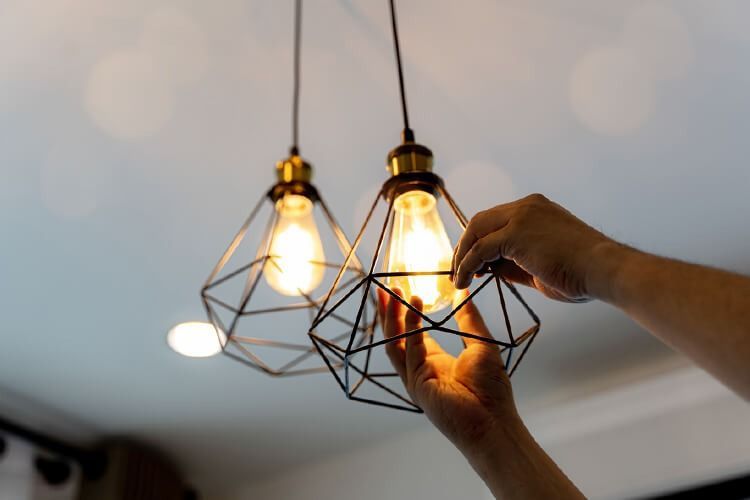 Hands adjusting a modern pendant light with geometric cage design; overhead view.