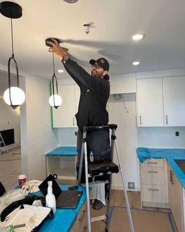 Man on stepladder installing ceiling light fixture in a kitchen.