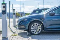 Blue electric car charging at a station, with a charging cable connected. Sunny outdoor setting.