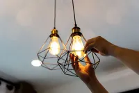 Hands adjusting a geometric pendant light with an exposed bulb.