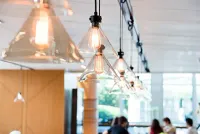Triangular glass pendant lights illuminate a dining area with people seated at tables near a window.