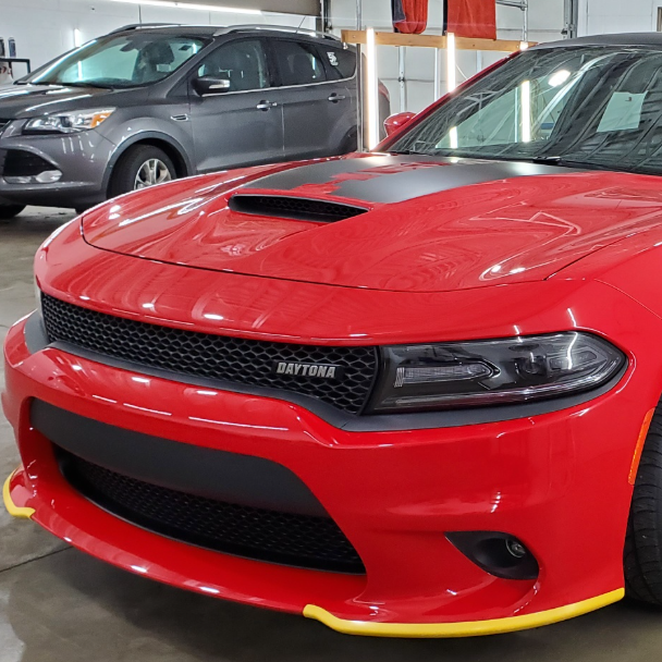 A blue car is parked in a garage next to a red car.