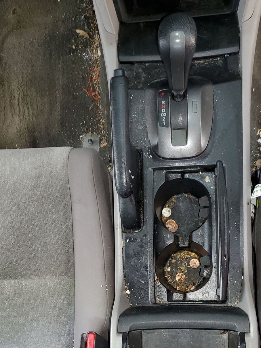 A dirty car console with two cup holders and a shifter