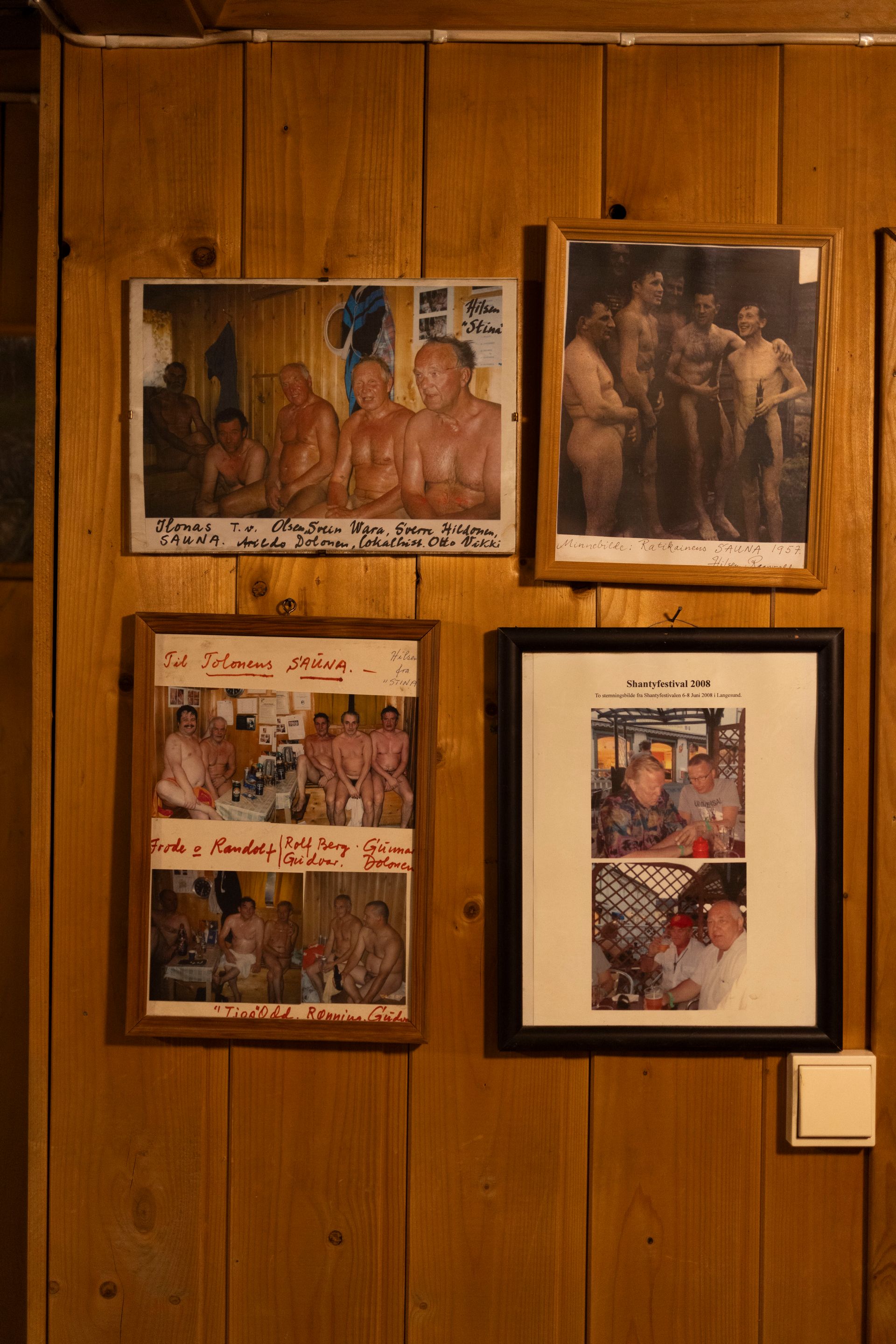 En trevegg i en sauna med flere innrammede bilder av saunaglade folk.