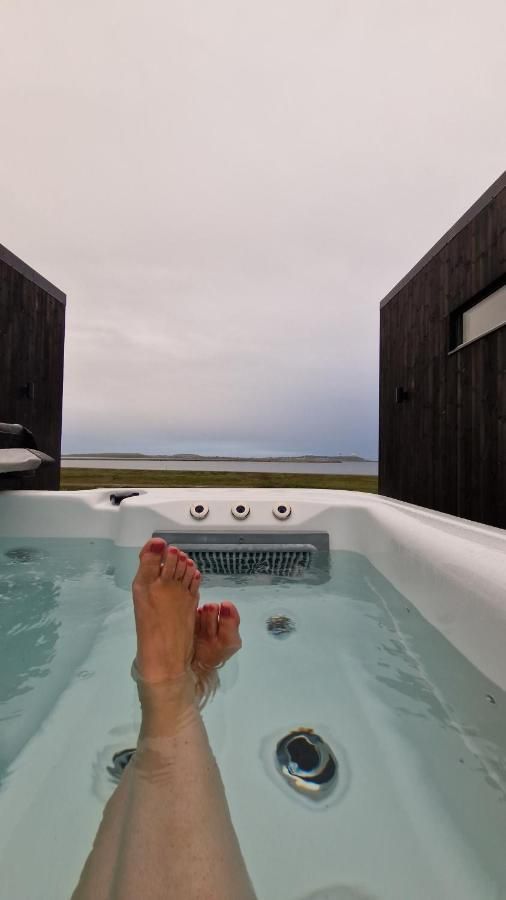 En person sitter i en jacuzzi med beina strekt ut og i kryss i selskap med Varangerfjordutsikt.