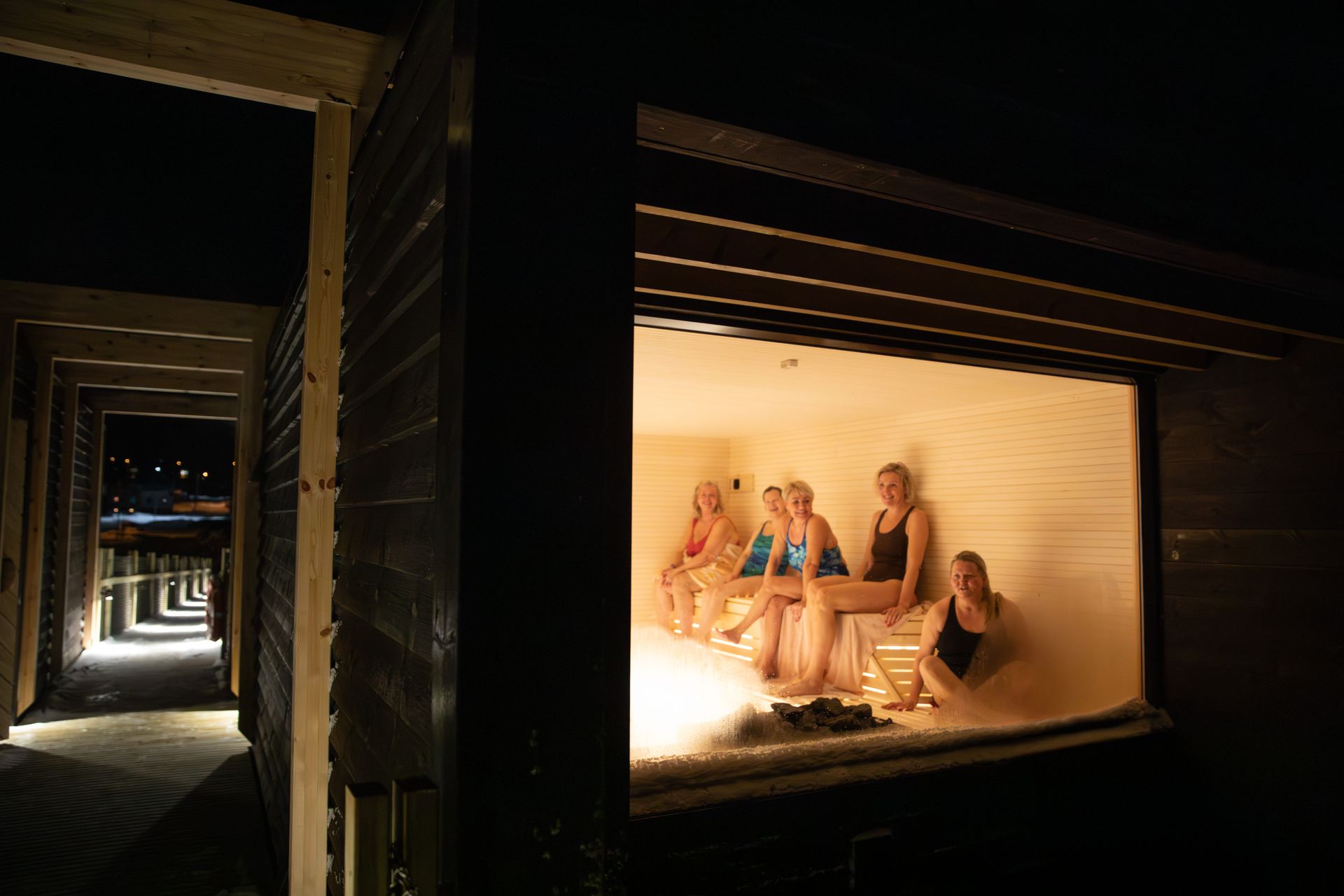 En tønnesauna i arktisk vinterlandskap, i vinduets refleksjon kan man se solnedgang.