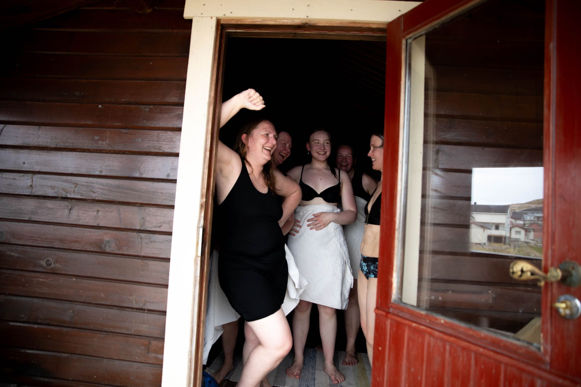 Flere kvinner står i åpningen av en sauna, de smiler og ler.