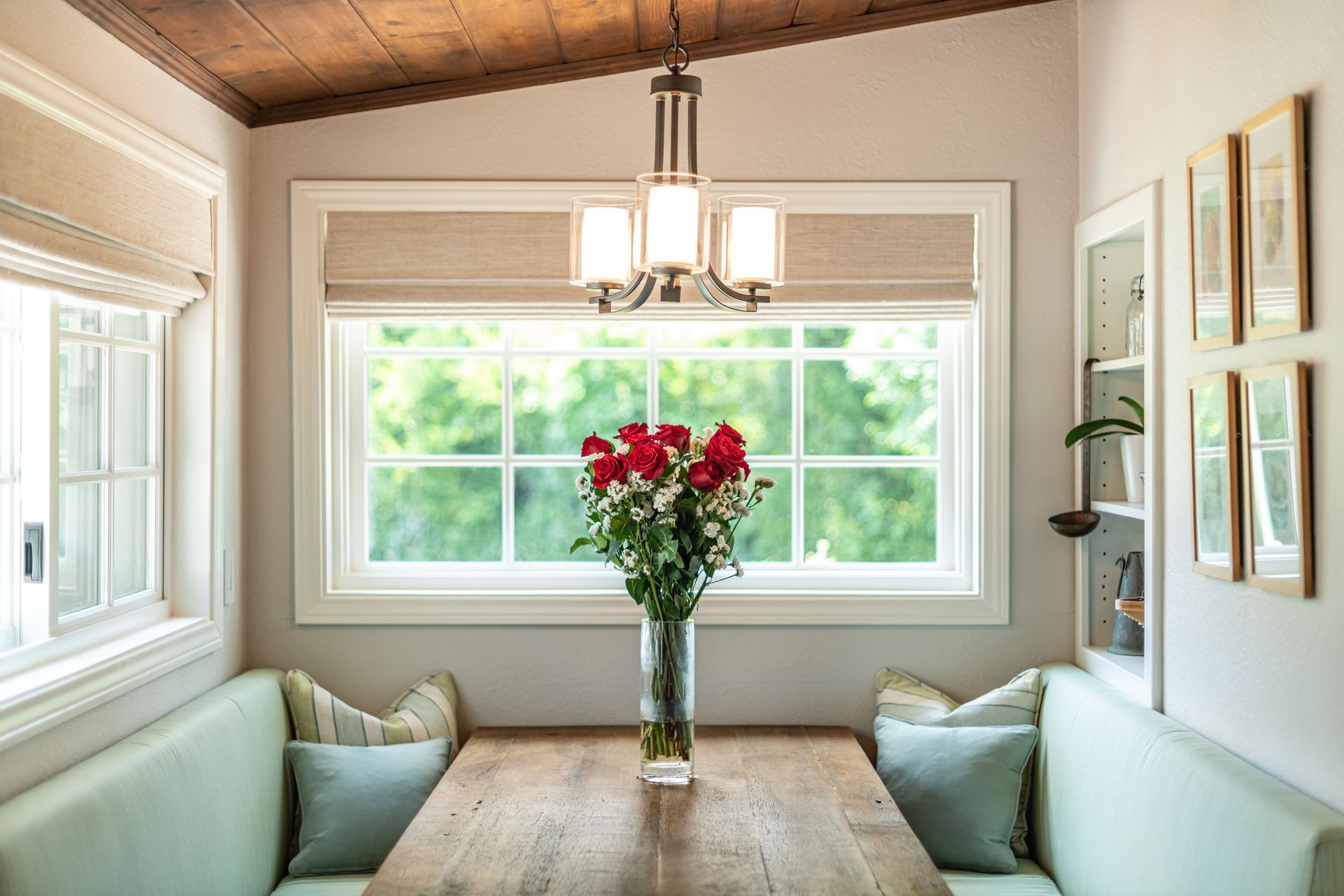 A dining room table with a vase of flowers on it in front of a window.