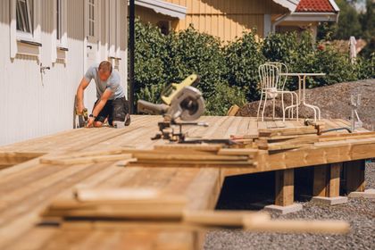 A man is working on a wooden deck in front of a house.