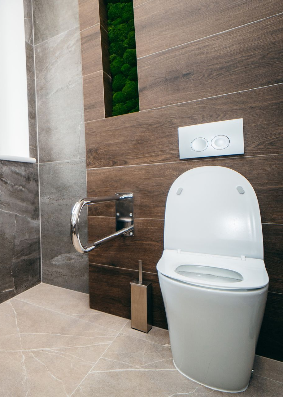 Modern bathroom with white toilet, brushed metal accessories, brown and gray tile, and a green moss accent.