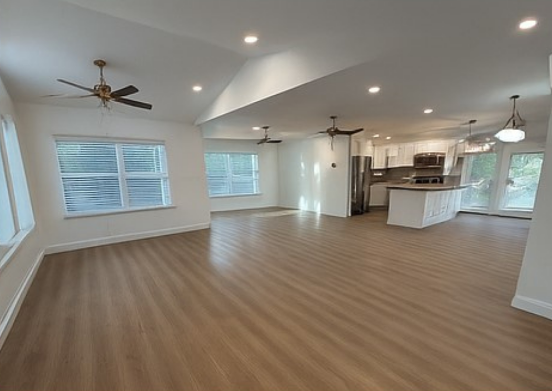 Open-concept living space with light wood floors, white walls, and a kitchen with stainless steel appliances.