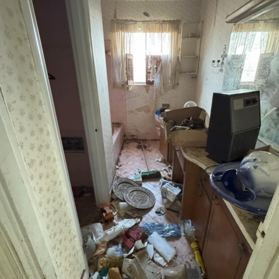 Messy bathroom with debris on the floor and countertops; visible window and open door.