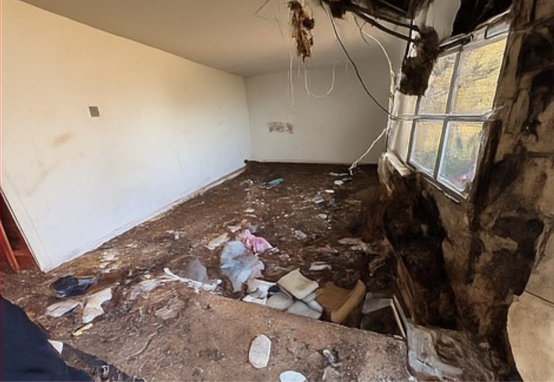 Interior room with significant damage; debris covers the floor, wall, and ceiling. A window is partially visible.