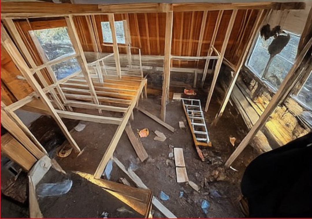 Interior view of a building under construction, featuring wooden framing, stairs, and debris on the floor.