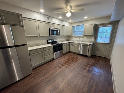 Modern kitchen with stainless steel appliances, gray cabinets, white countertops, and wood-look flooring.