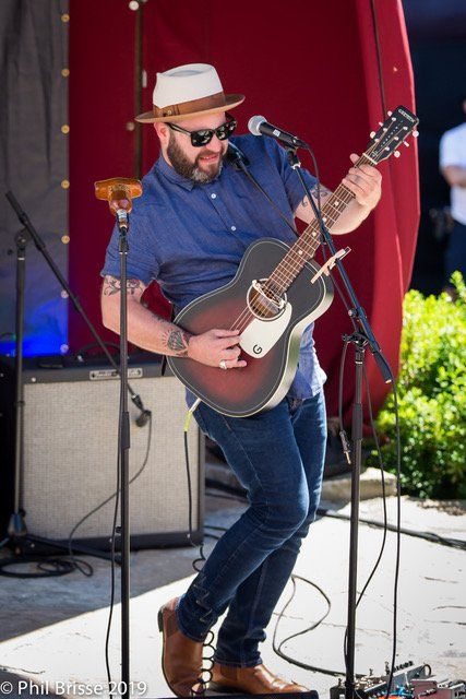 Steve Marriner playing guitar wearing sun glasses and sun hat on stage