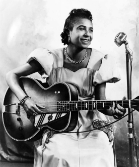 African American woman sitting down playing a guitar