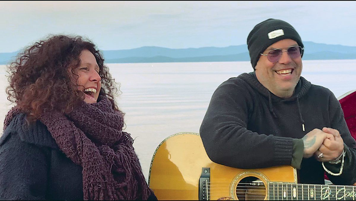 Angel Forrest and Denis Coulombe looking a little chilly sitting by a lake with mountains in the background