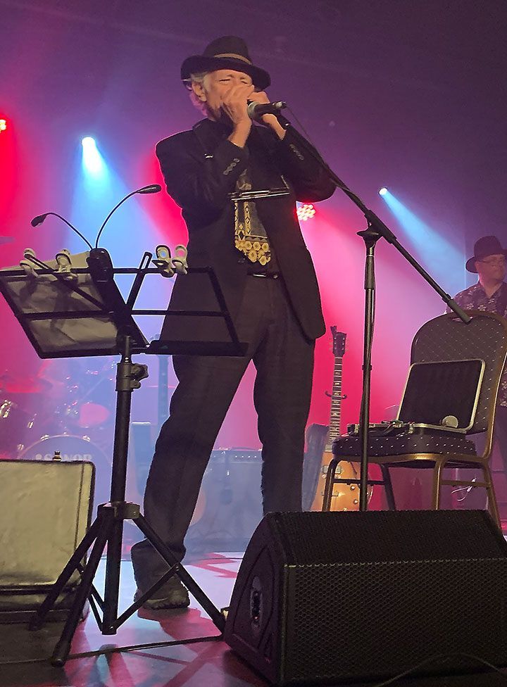 Jay Sewall playing harmonica on stage with microphones and  musical instruments all around him