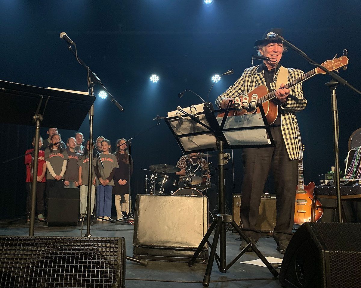 Jay Sewall playing guitar on stage with a small group of children of about 8-9 years old singing along