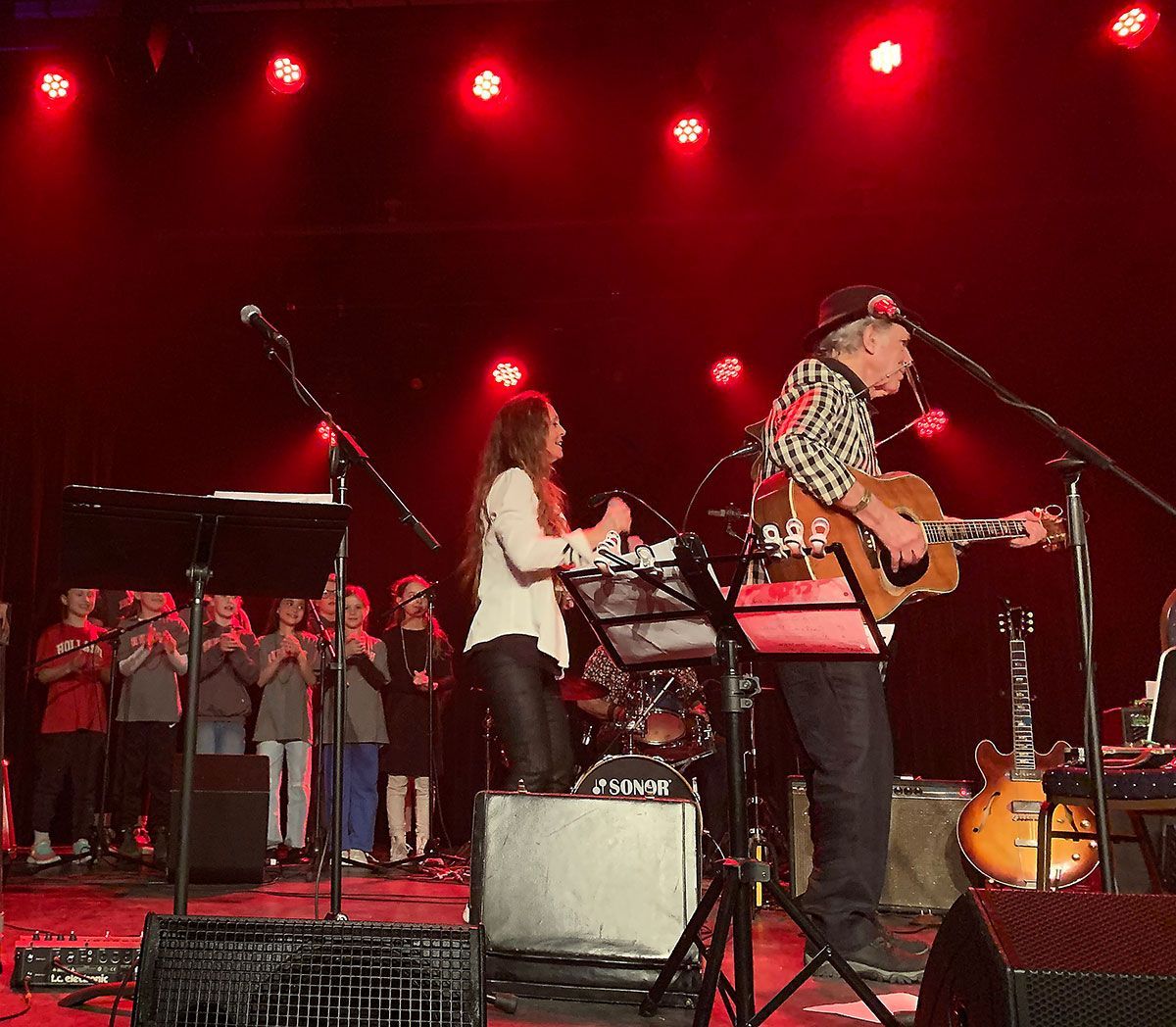 Jay Sewall and a woman singing with a small group of children of about 8 or 9 up on stage in the background