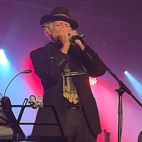 Jay Sewall playing harmonica on a stage lit with blue and pink lights