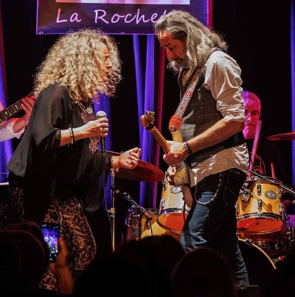 Woman on stage holding a microphone, face to face with a guitarist