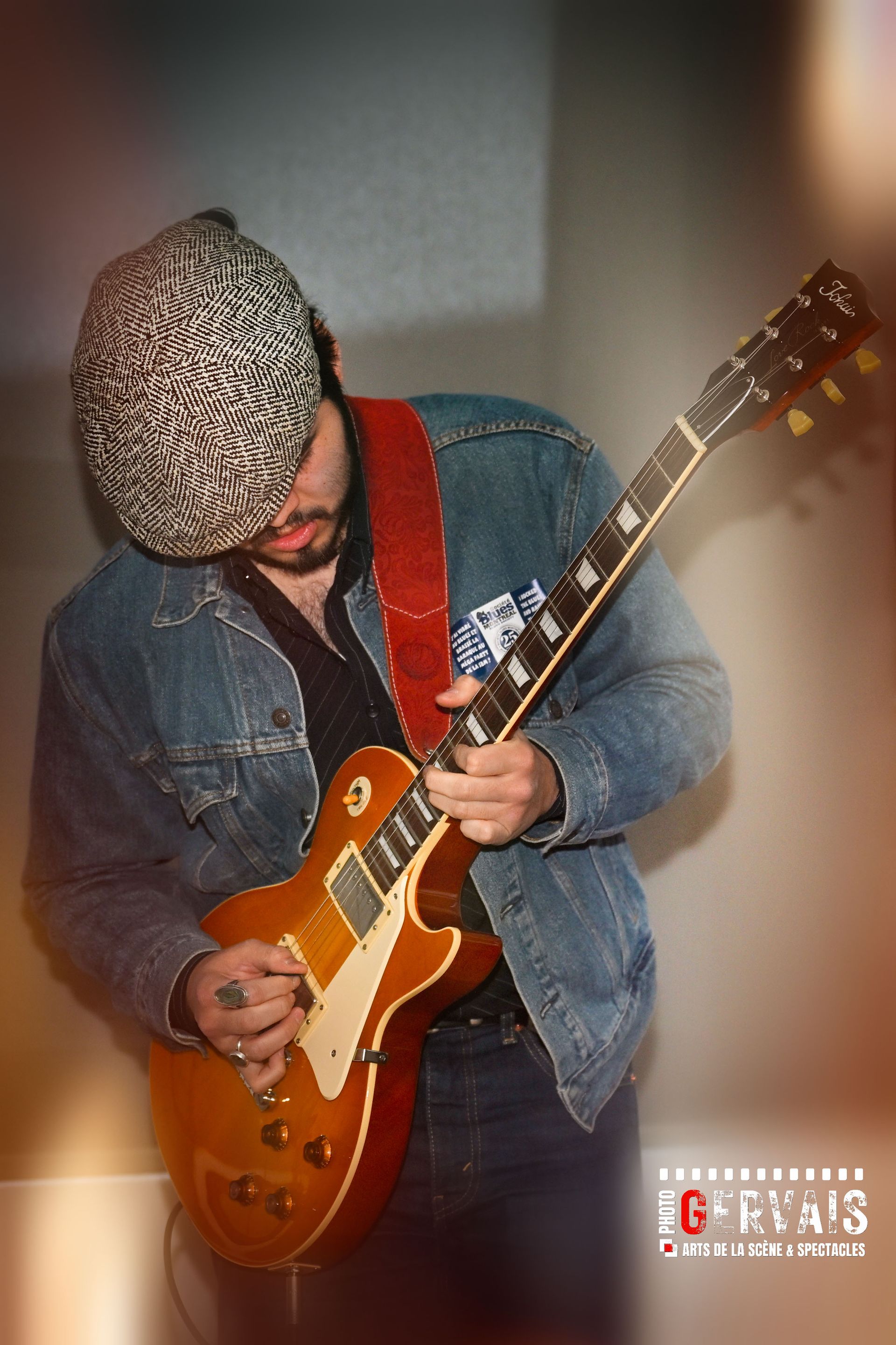 A man in a cap and wearing a jean jacket playing guitar