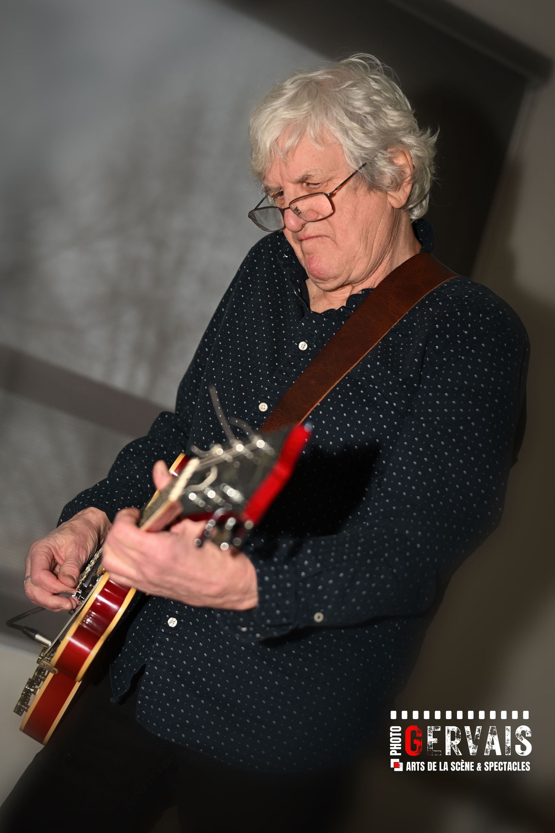 A man wearing glasses playing a red electric guitar