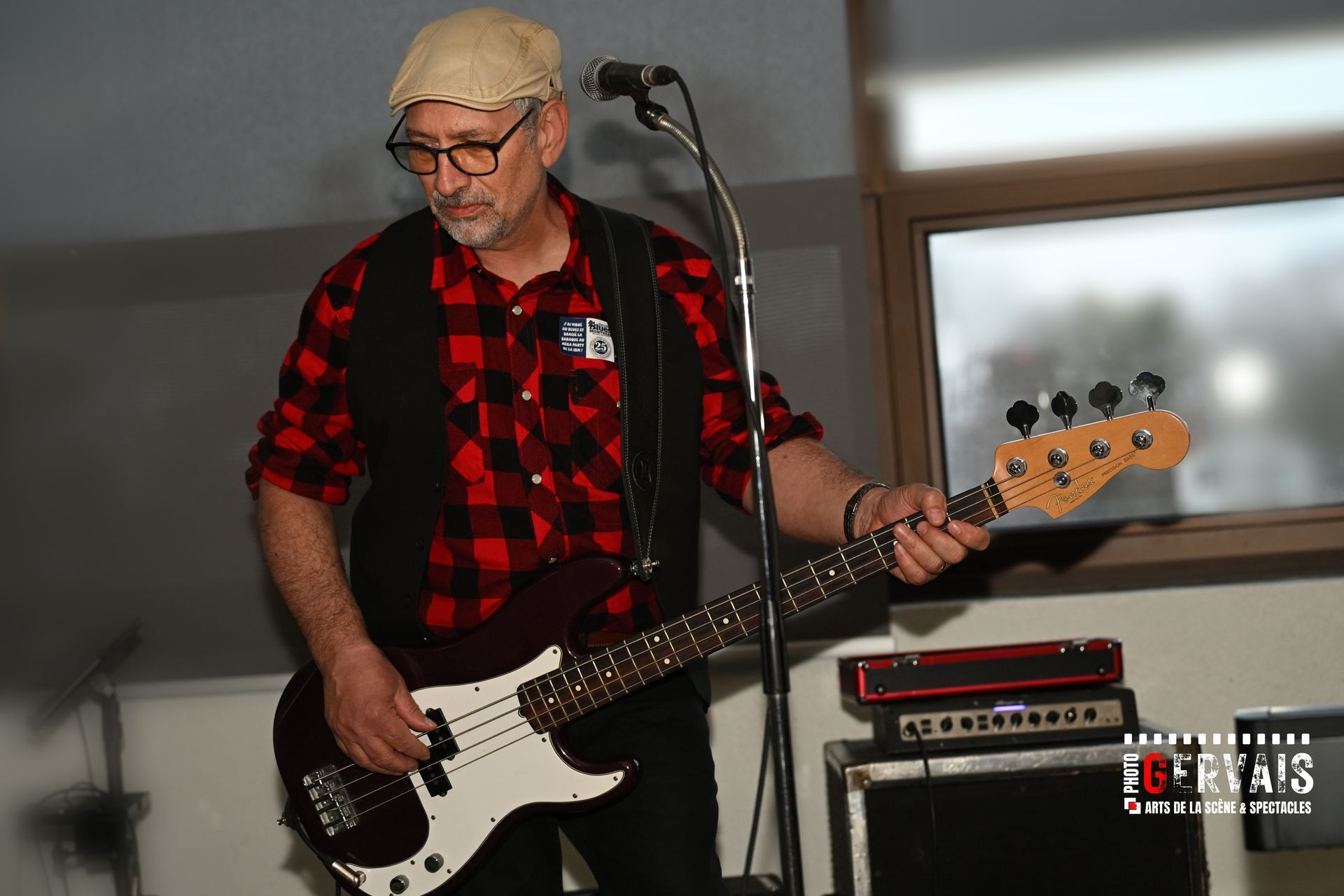 A man wearing a cap and a red and black checkered shirt playing a base guitar