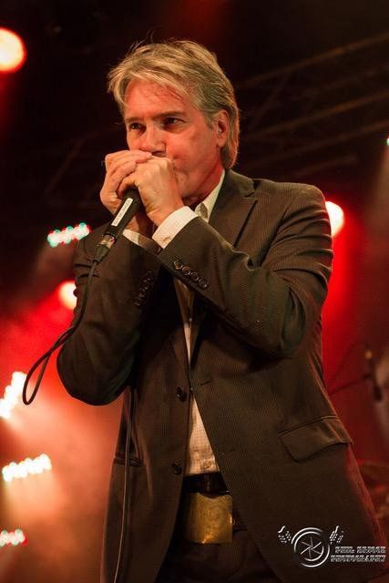 Guy Bélanger, looking distinguished and as handsome as ever with his premature white hair, on stage blowing his harmonica.