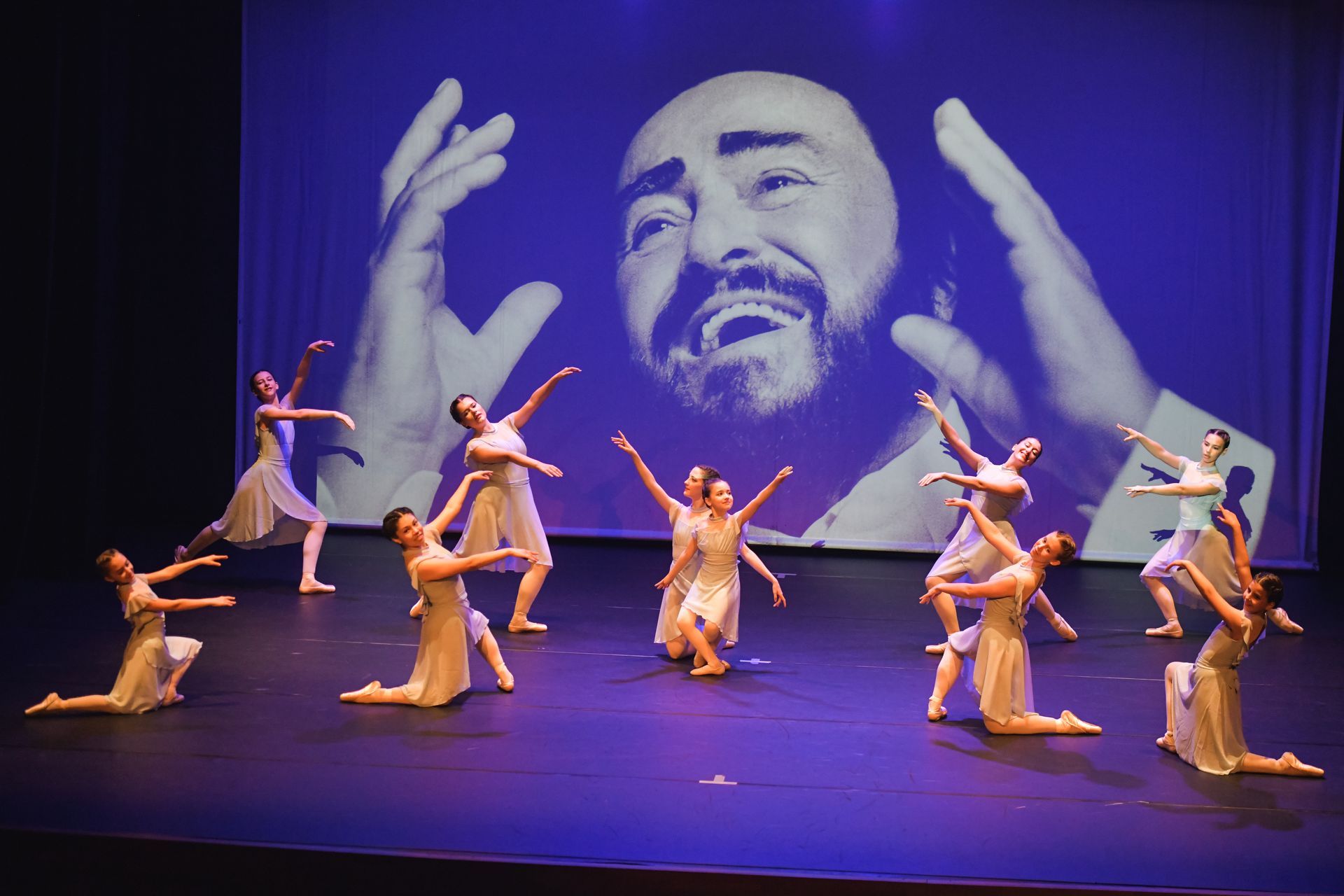 Un gruppo di ballerini si esibisce su un palco davanti a un grande schermo su cui è raffigurata l'immagine di un uomo.