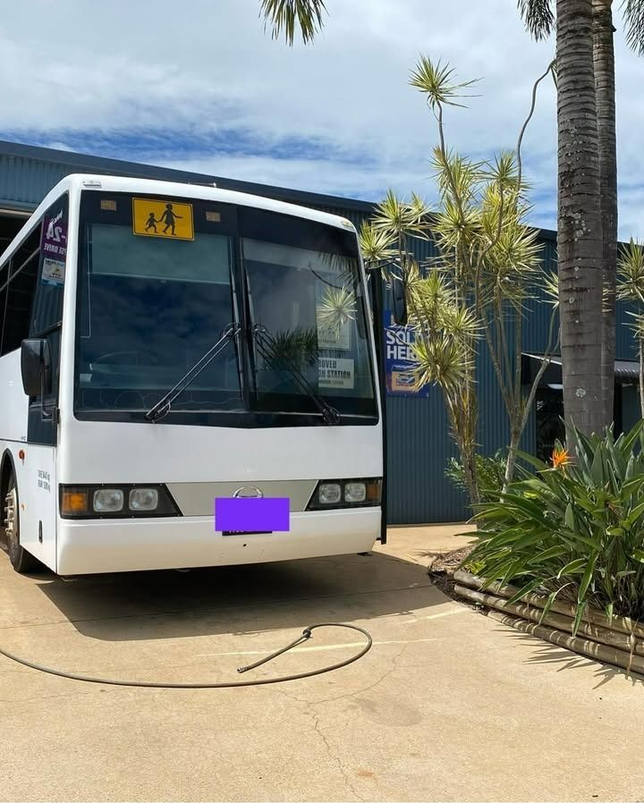 White School Bus Parked in Front of a Building With a School Zone Sign — Atherton Mechanical Services in Atherton, QLD