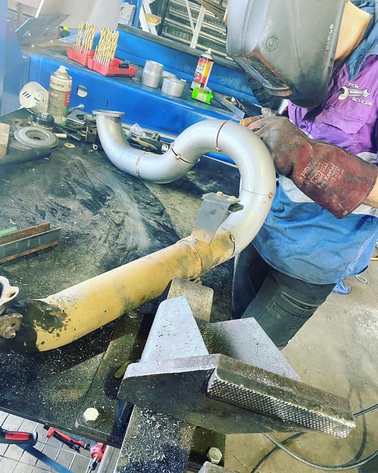 A Person Welding a Curved Metal Pipe in a Workshop — Atherton Mechanical Services in Mareeba, QLD
