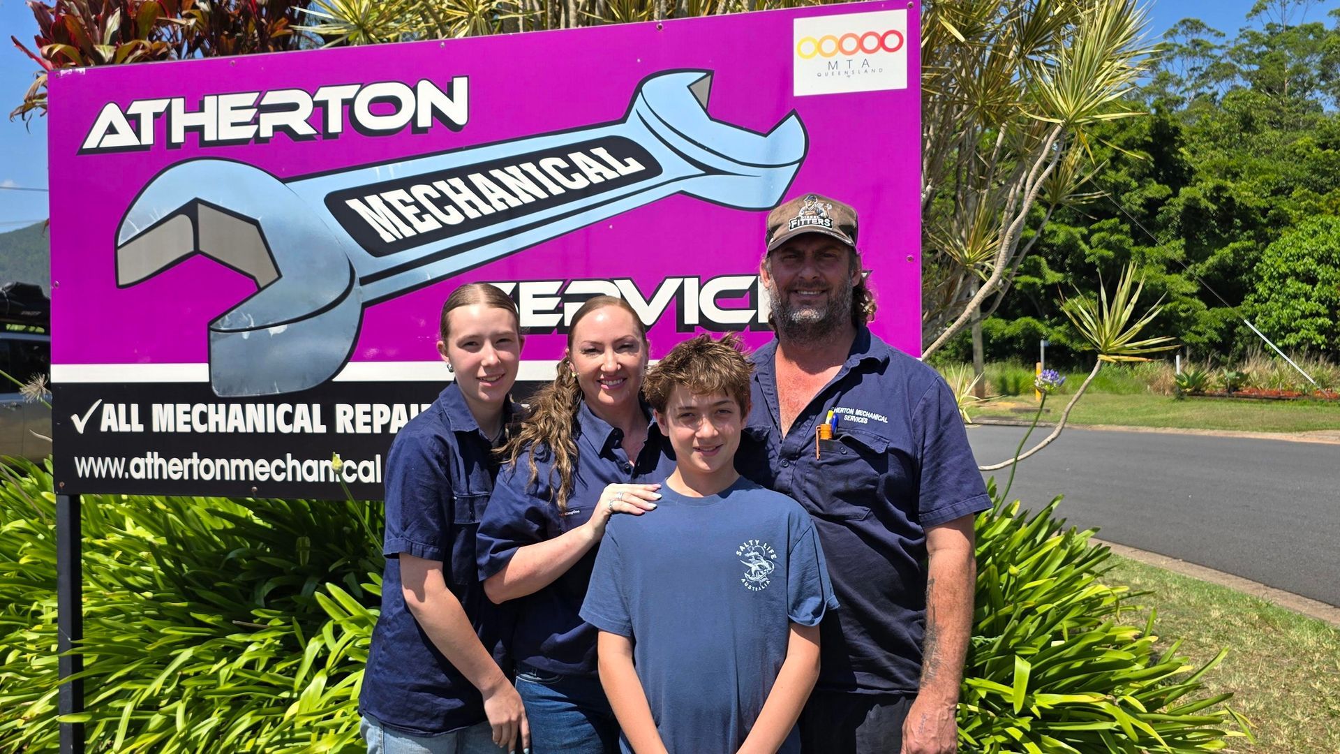 Family Stands In Front Of A Mechanic Shop Sign. Mother Holding Baby, Father Holding Toddler — Atherton Mechanical Services in Atherton, QLD