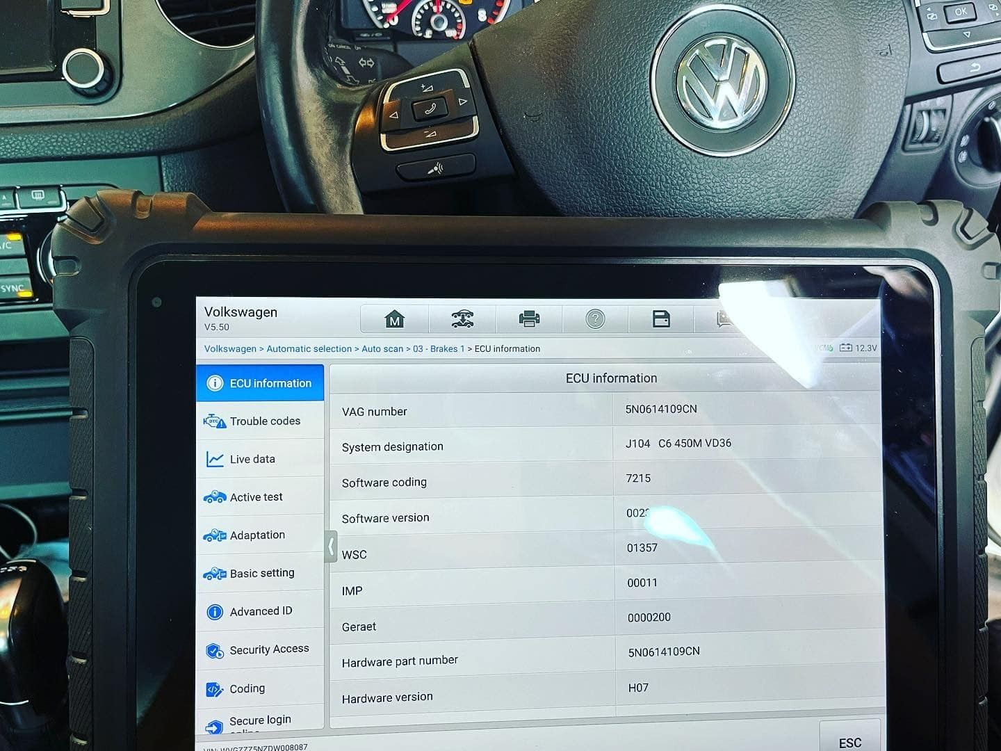 A diagnostic tablet displaying car data next to a VW steering wheel. In a car.