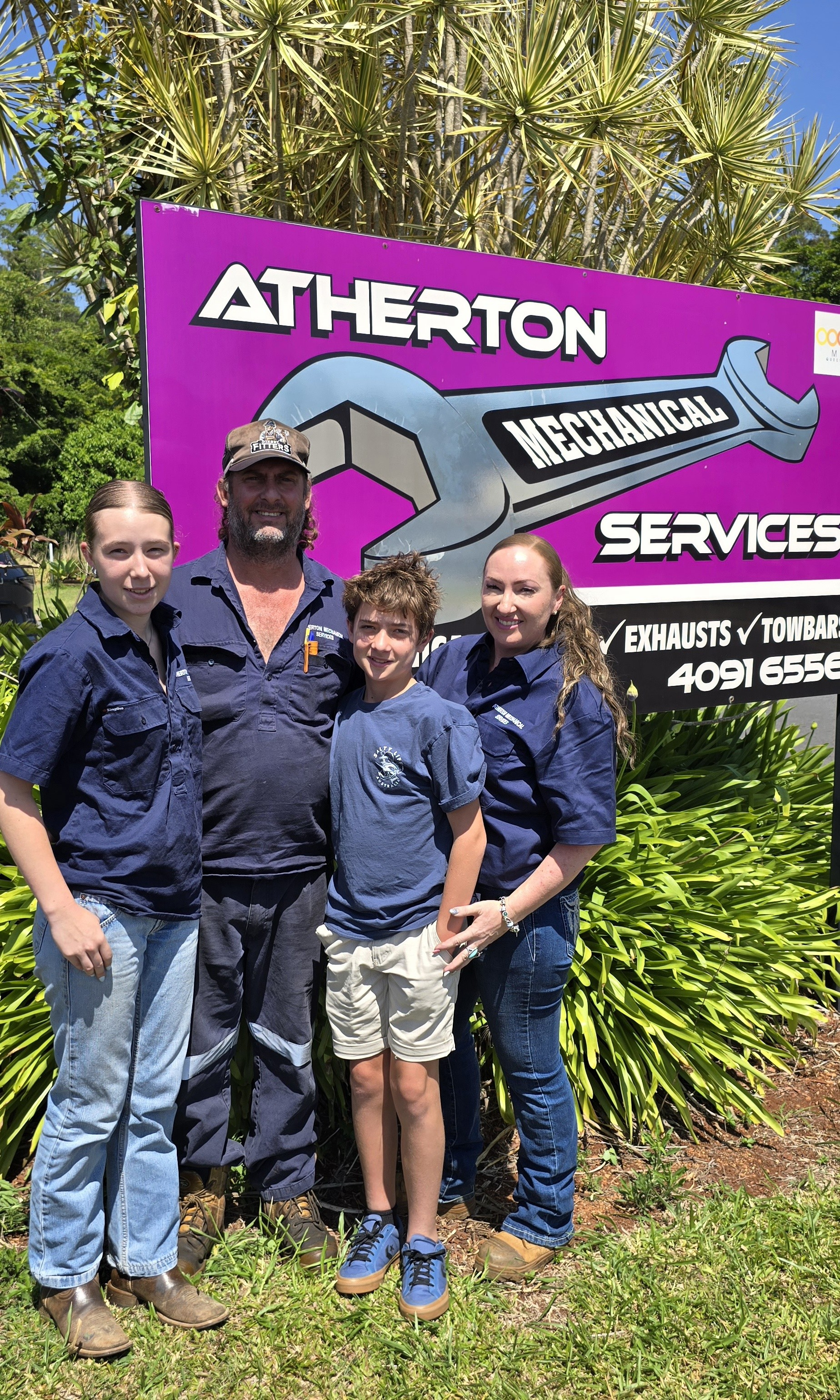 Family Stands In Front Of A Mechanic Shop Sign. Mother Holding Baby, Father Holding Toddler — Atherton Mechanical Services in Atherton, QLD