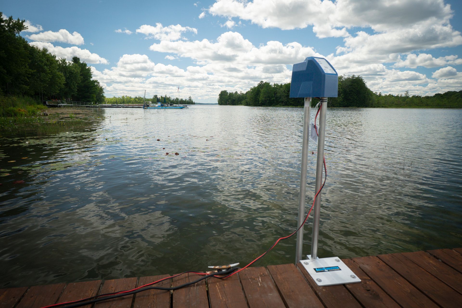 A water quality monitoring device on a wooden dock, blue and silver, measuring lake water.