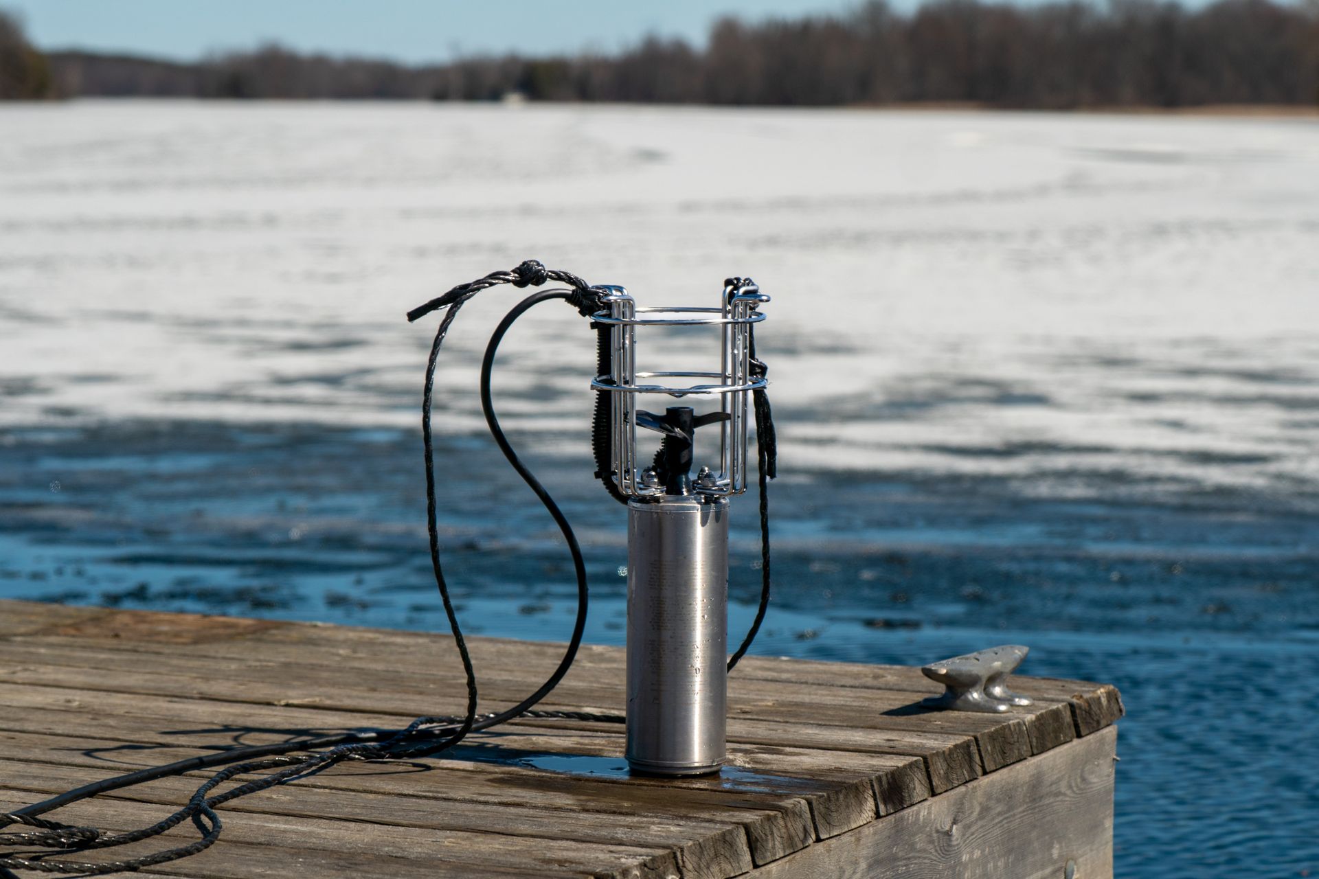 A silver de-icer/watercirculator on a wooden dock with a snowy lake in the background.