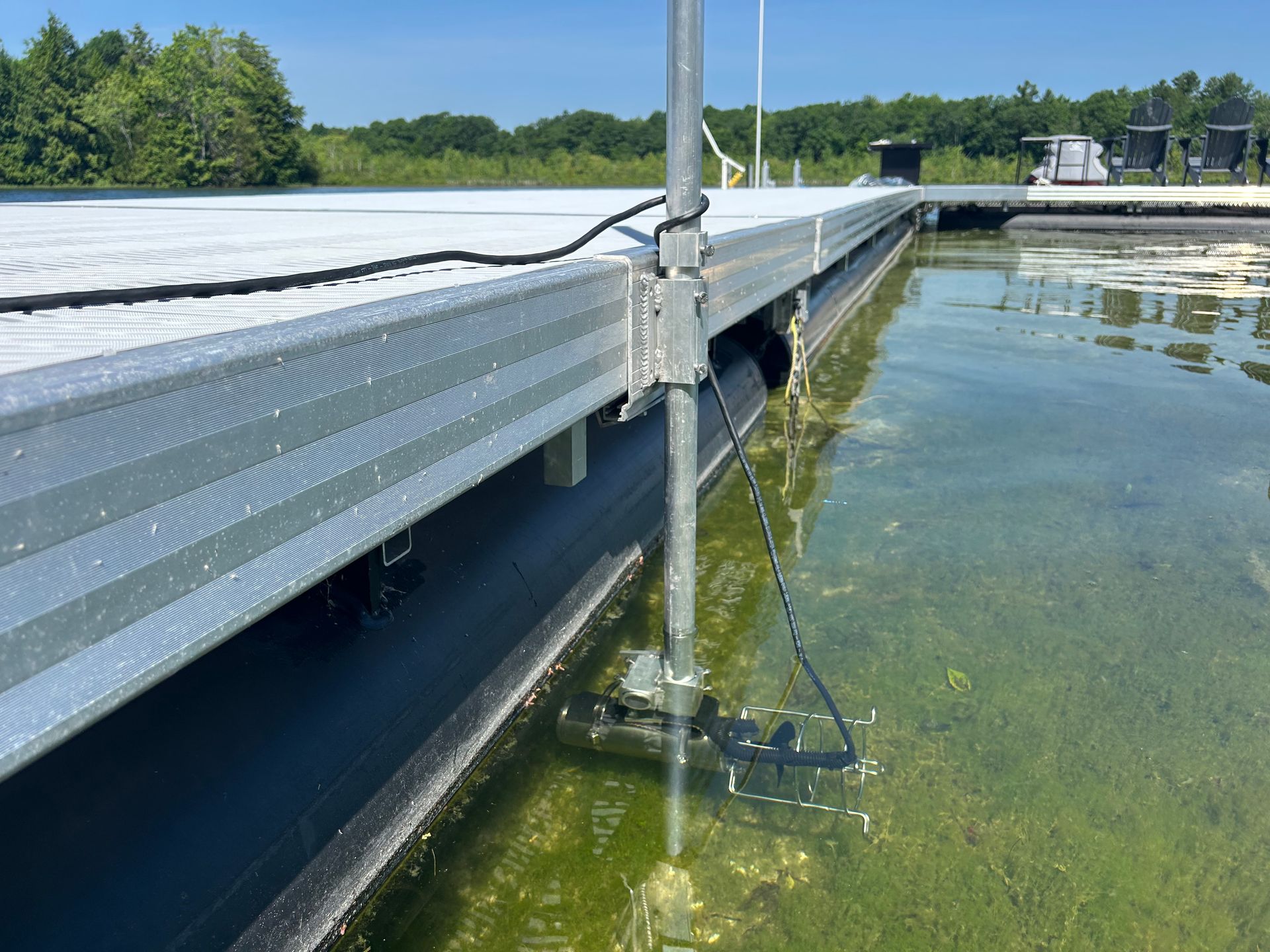 A metal dock extends over water with a submerged pole and algae visible below.
