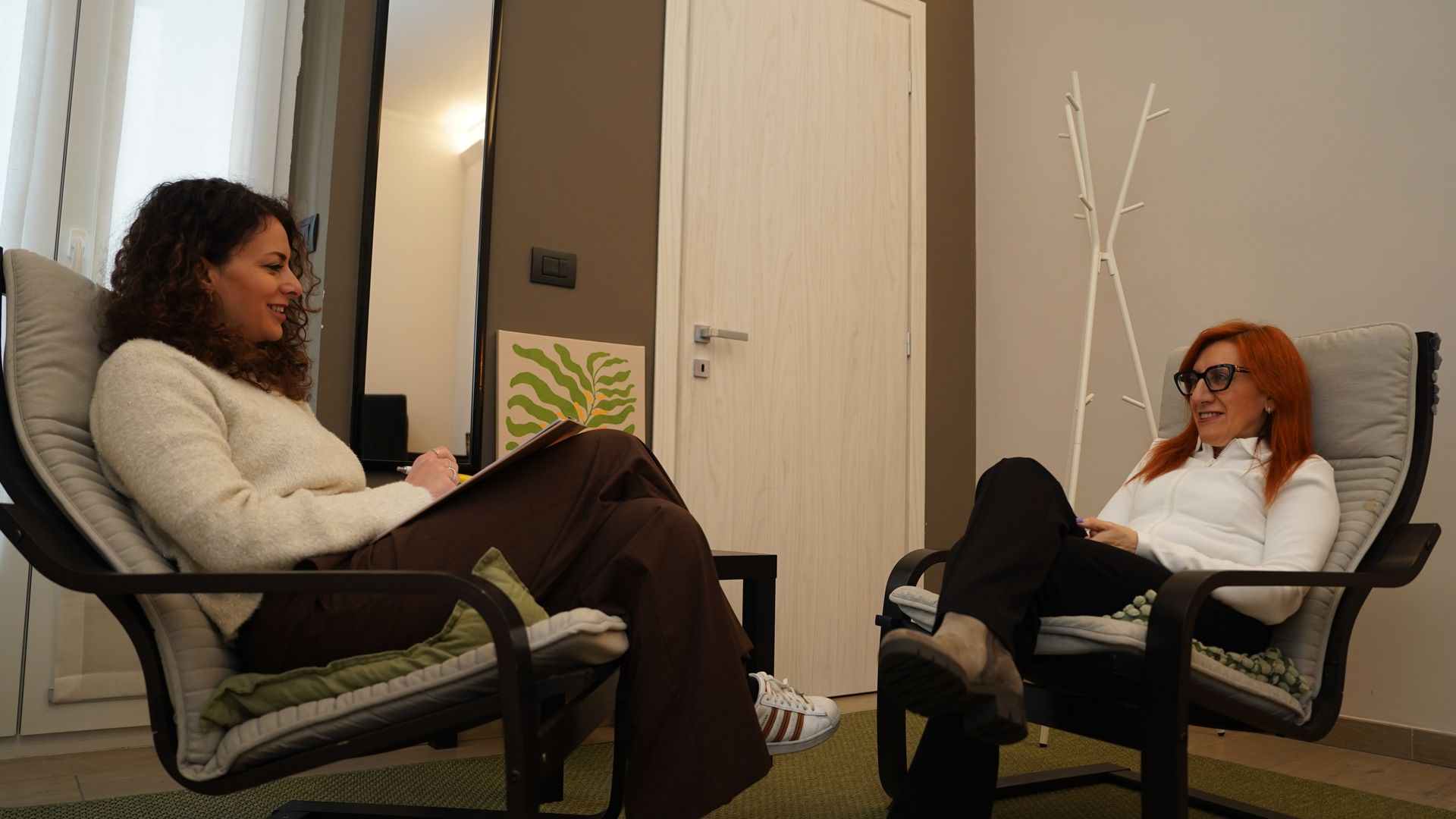 Due donne sono sedute su delle sedie e parlano tra loro in una stanza.