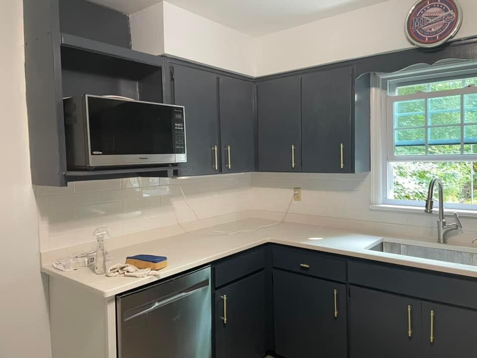 A modern kitchen with dark gray cabinets, white countertops, a built-in microwave, a stainless steel sink, and a window.